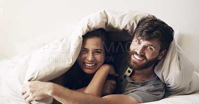 Buy stock photo Shot of a happy young couple covering themselves with a blanket on the bed at home