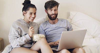 Buy stock photo Shot of a happy young couple using a laptop and eating popcorn while relaxing on the bed at home