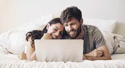 Buy stock photo Shot of a happy young couple using a laptop while relaxing on the bed at home