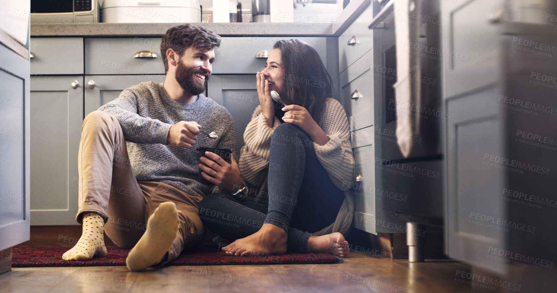 Buy stock photo Shot of a happy young couple sharing a tub of ice cream in their kitchen at home