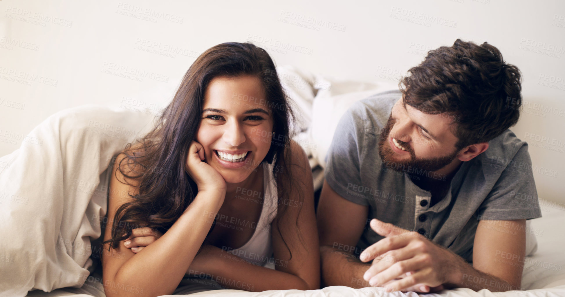 Buy stock photo Shot of a happy young couple relaxing in bed together at home