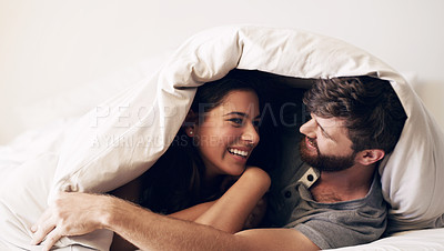 Buy stock photo Shot of a happy young couple covering themselves with a blanket on the bed at home