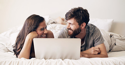 Buy stock photo Shot of a happy young couple using a laptop while relaxing on the bed at home