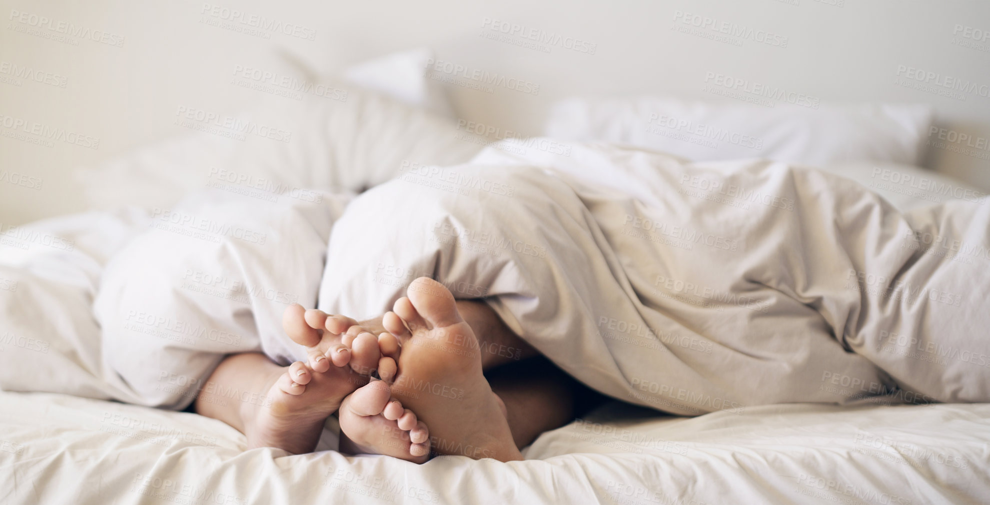 Buy stock photo Shot of a couple’s feet poking out from under the bed sheets