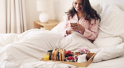 Buy stock photo Shot of a beautiful young woman using a smartphone while having breakfast in bed at home
