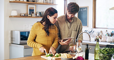 Buy stock photo Shot of a young couple using a digital tablet while preparing a meal at home