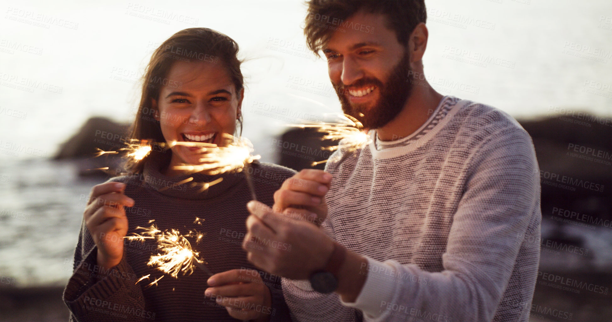 Buy stock photo Sparkle, fireworks and people on beach celebrate with happiness on holiday or vacation in summer. Fire, sparks and couple at ocean sunset and excited for countdown to new year at party or event 