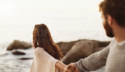 Buy stock photo Shot of a young woman pulling her boyfriend by the hand while walking on the beach
