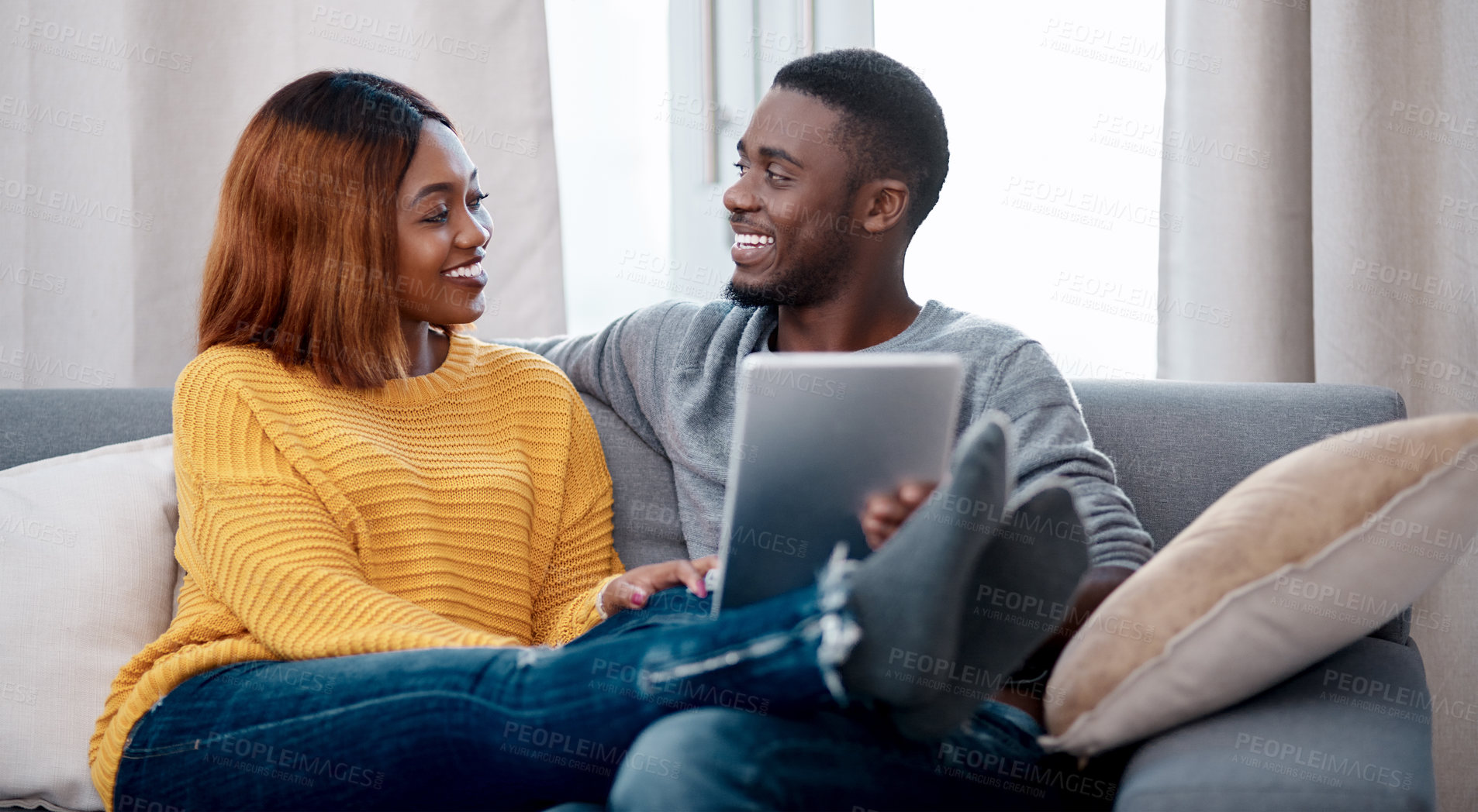 Buy stock photo Shot of a young couple using a digital tablet while relaxing at home