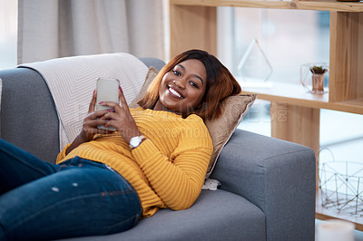 Buy stock photo Shot of an attractive young woman using her cellphone while relaxing on the sofa at home