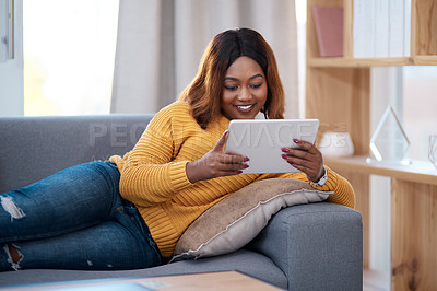 Buy stock photo Shot of an attractive young woman using a digital tablet while relaxing at home