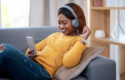 Buy stock photo Shot of an attractive young woman wearing headphones while using her cellphone