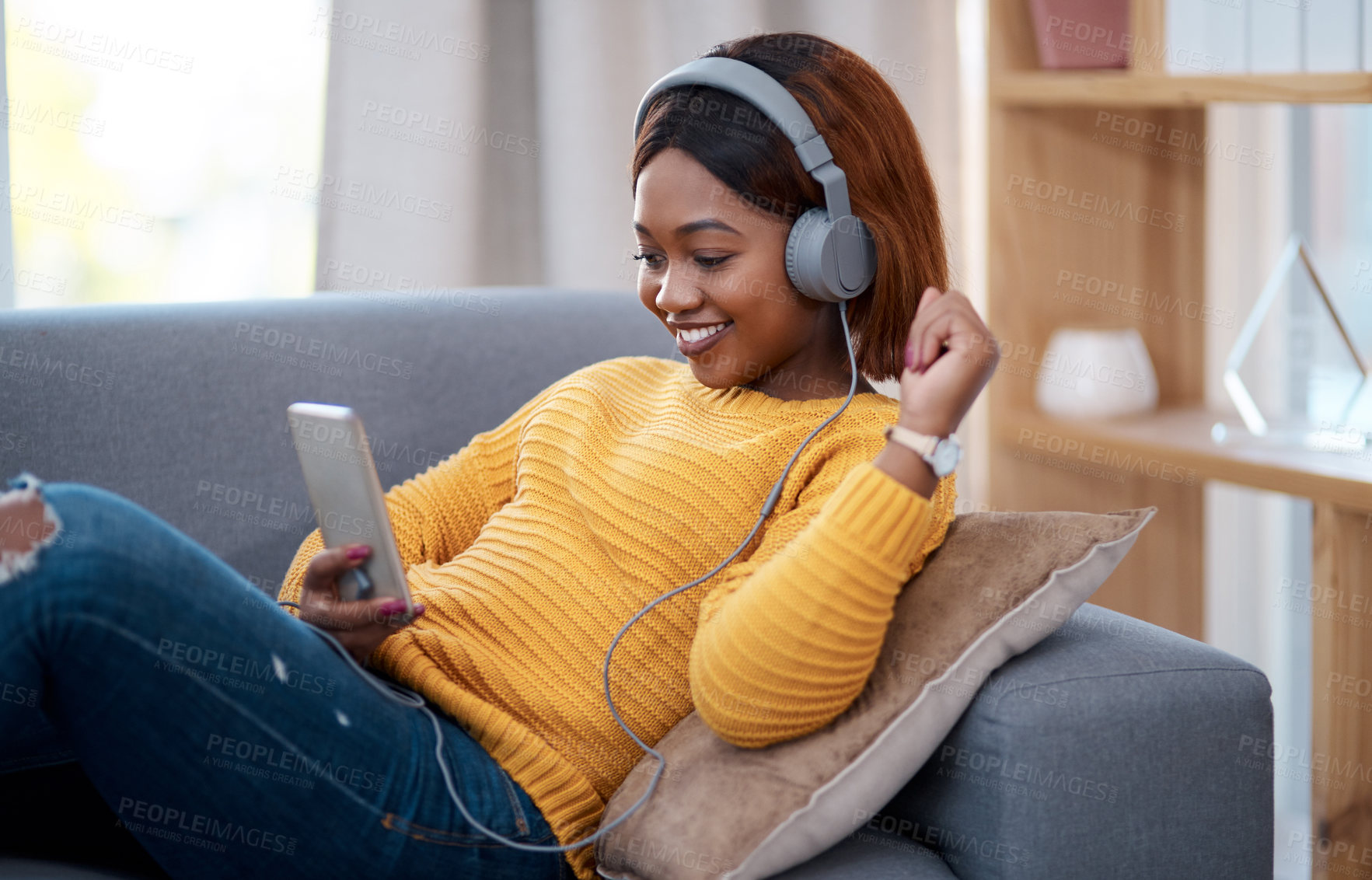 Buy stock photo Shot of an attractive young woman wearing headphones while using her cellphone