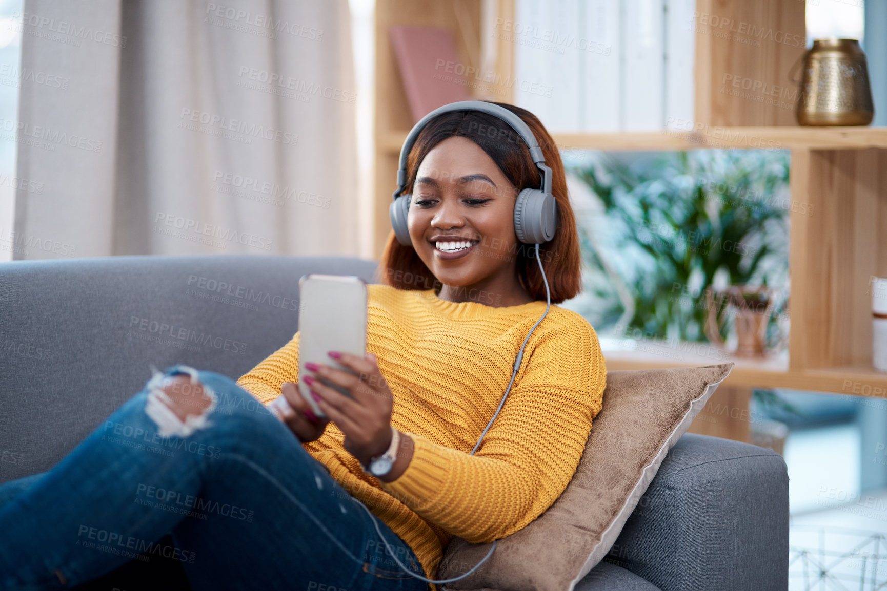 Buy stock photo Relax, phone and music with a black woman on a sofa in the living room of her home streaming audio through headphones. Mobile, freedom and time off with a happy young female listening to the radio