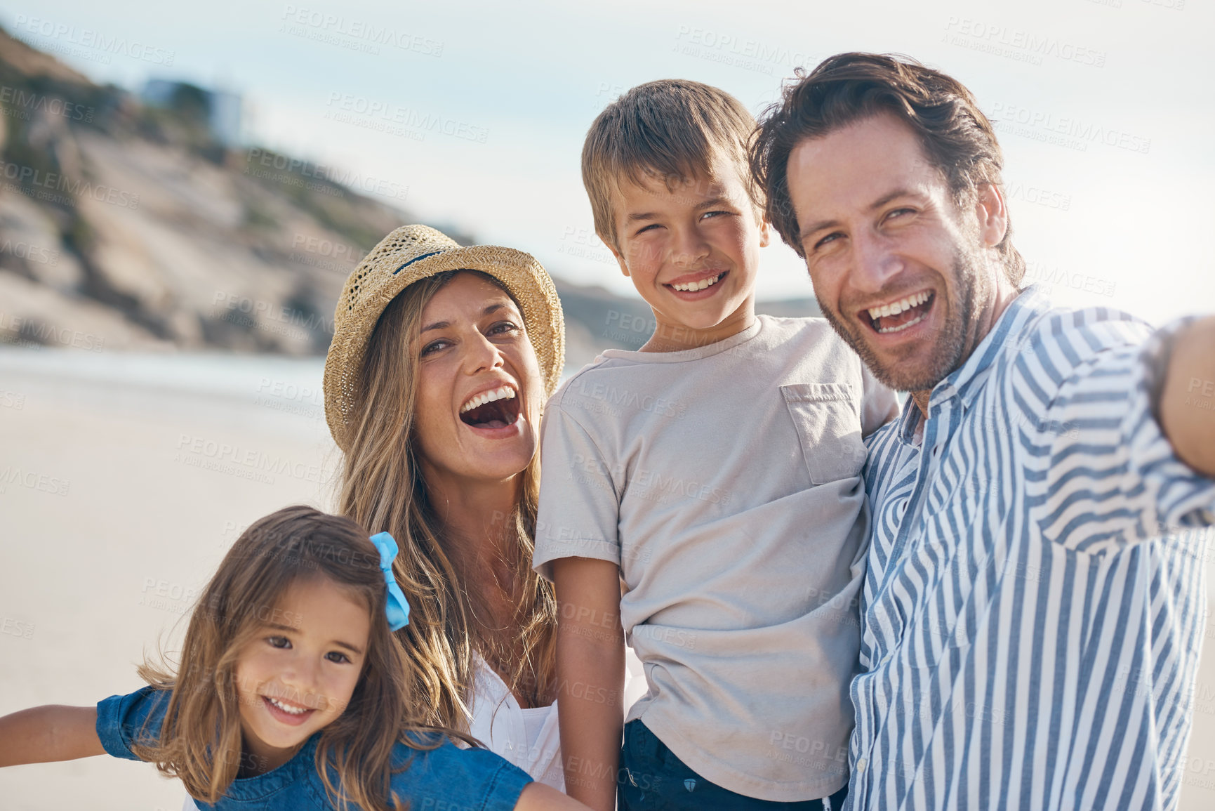 Buy stock photo Cropped portrait of an affectionate couple carrying their two children and posing for a selfie on the beach