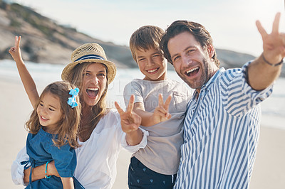 Buy stock photo Cropped portrait of a happy couple carrying their two children and making peace sign gestures on the beach