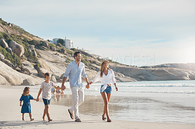 Buy stock photo Full length shot of a happy couple holding hands with their two young children and walking along the beach