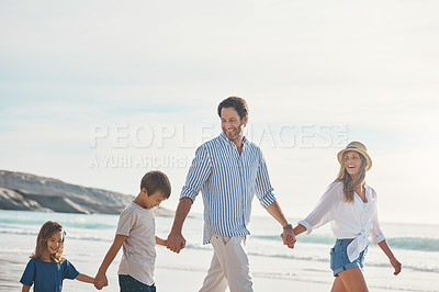 Buy stock photo Cropped shot of a happy couple holding hands with their two young children and walking along the beach