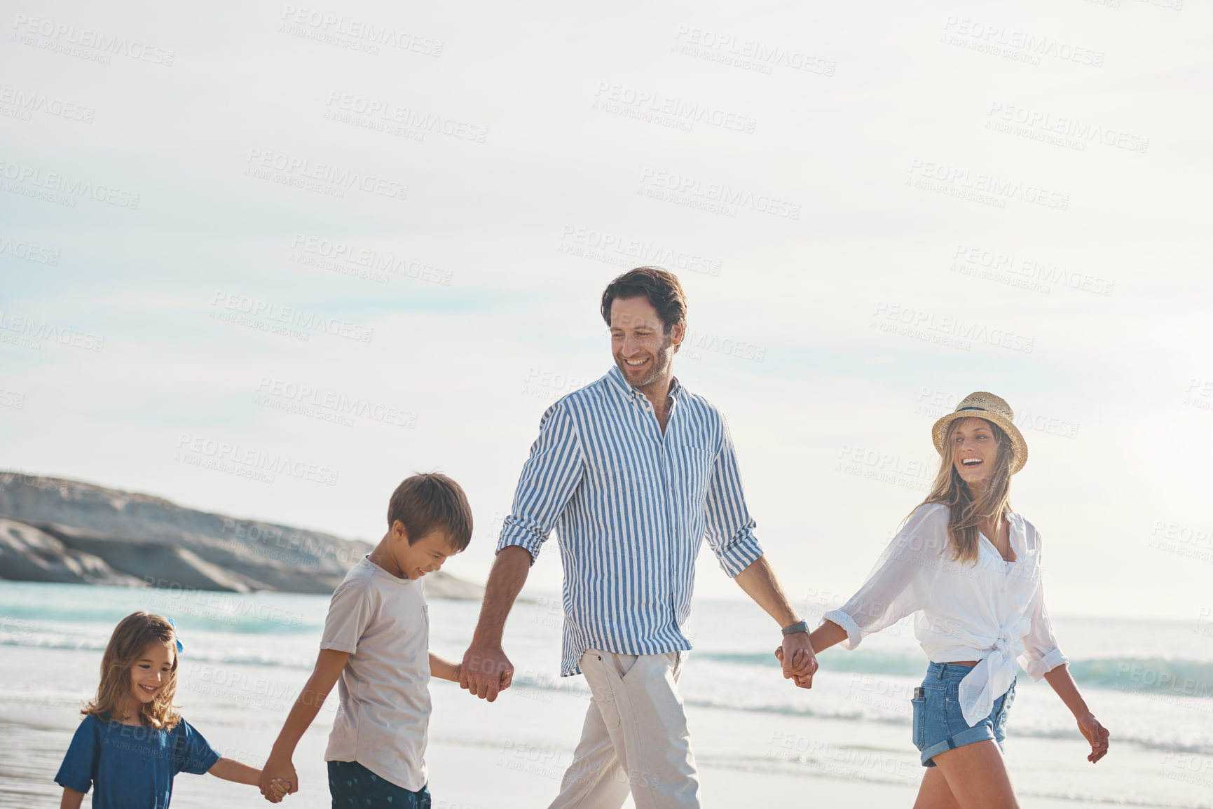 Buy stock photo Cropped shot of a happy couple holding hands with their two young children and walking along the beach