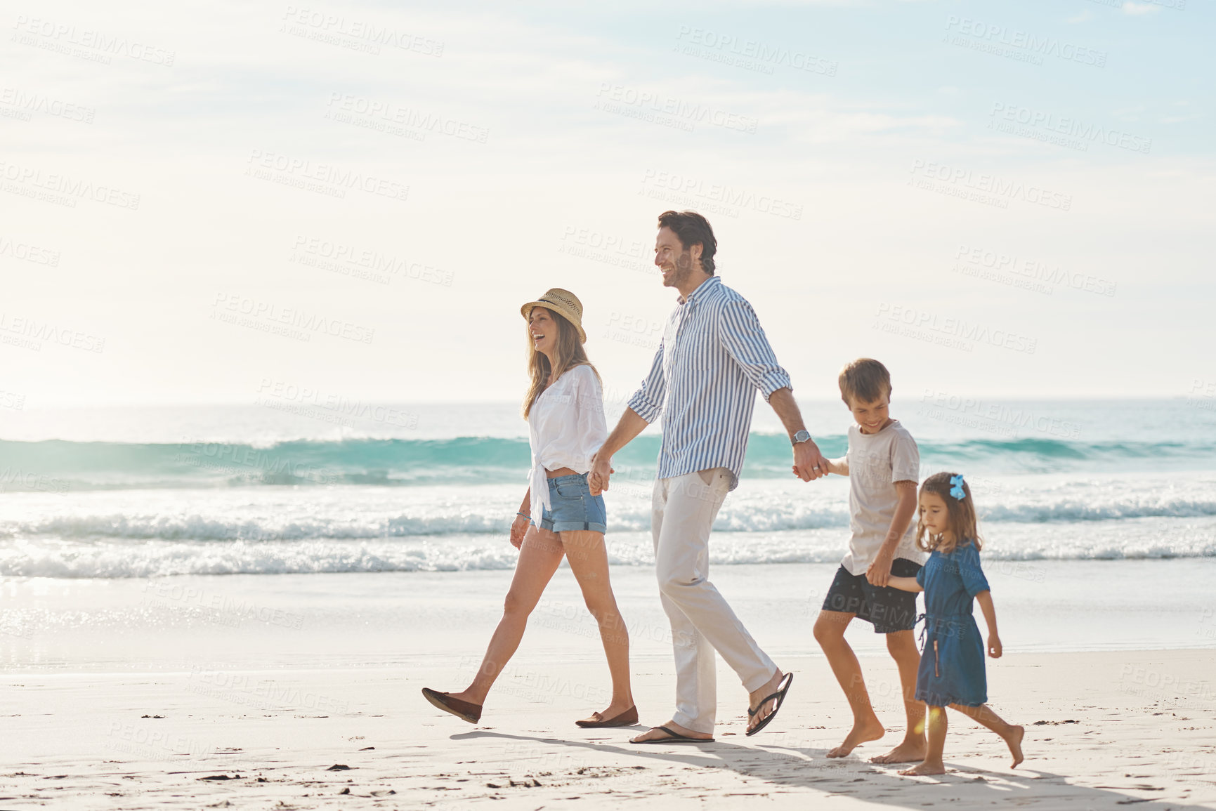 Buy stock photo Full length shot of a happy couple holding hands with their two young children and walking along the beach