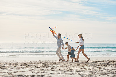Buy stock photo Full length shot of a happy couple holding hands with their children and walking along the beach with a kite