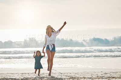 Buy stock photo Full length portrait of an affectionate young mother holding her daughter's hand and walking on the beach