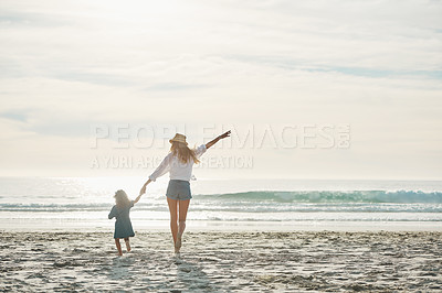 Buy stock photo Rearview shot of an affectionate young mother holding her daughter's hand and walking towards the sea during a day out