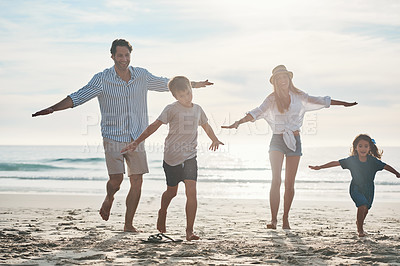 Buy stock photo Full length shot of a happy young couple enjoying a playful day out with their two children on the beach