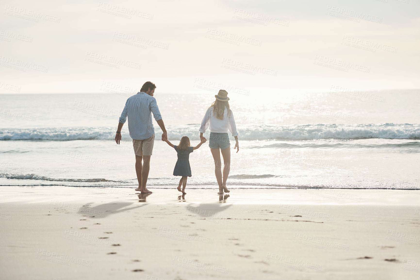 Buy stock photo Rearview shot of an unrecognizable couple holding hands with their little daughter and walking on the beach together