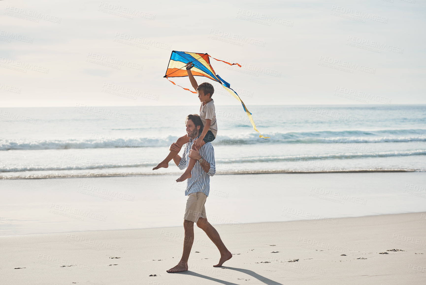 Buy stock photo Full length shot of a young boy being carried on his father's shoulders and holding a kite on the beach