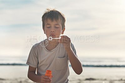 Buy stock photo Cropped shot of a young boy standing alone and blowing bubbles during a day on the beach