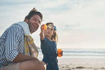 Buy stock photo Cropped shot of a playful mature father blowing bubbles with his daughter during a day out on the beach together