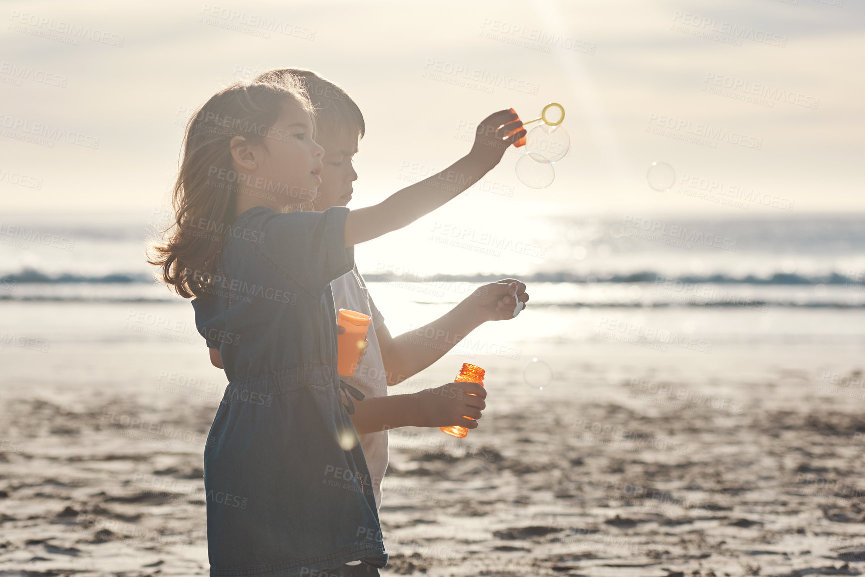 Buy stock photo Cropped shot of two young siblings standing together and blowing bubbles during a relaxing day on the beach