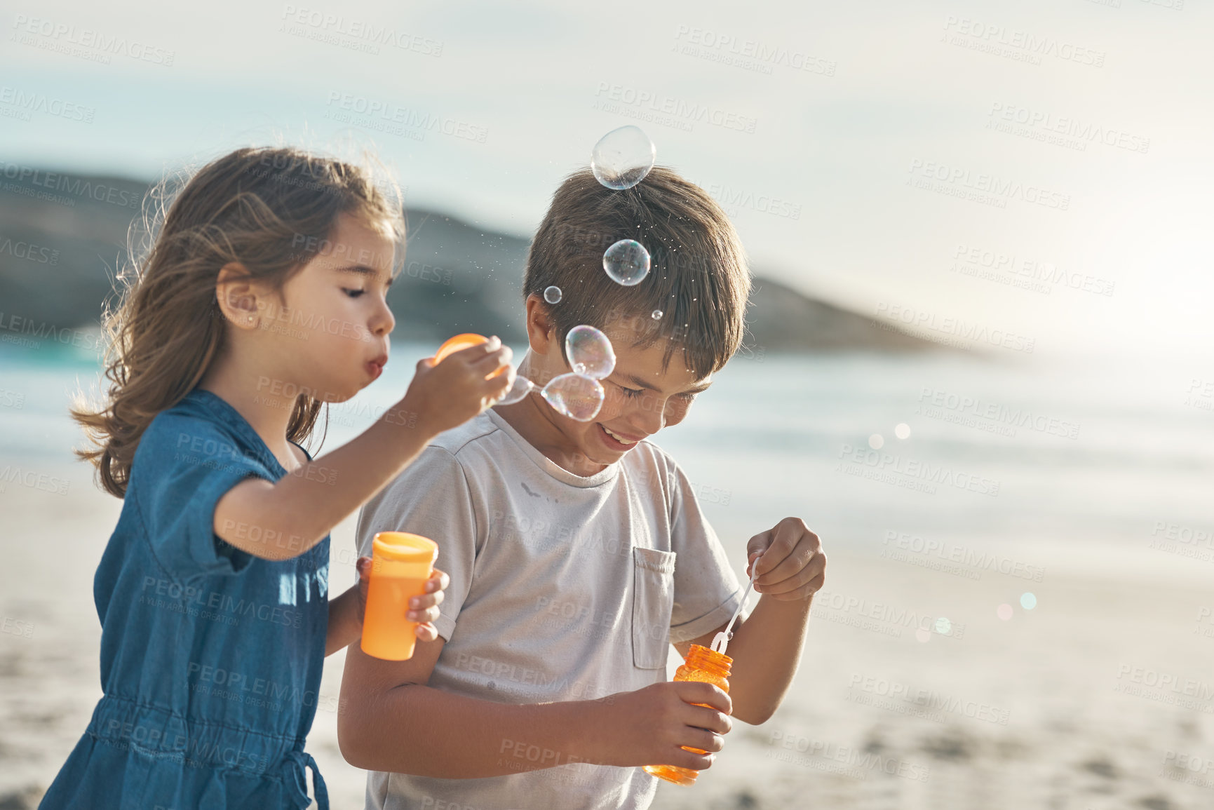 Buy stock photo Cropped shot of two young siblings standing together and blowing bubbles during a relaxing day on the beach