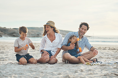 Buy stock photo Full length shot of a happy couple sitting with their two children who are blowing bubbles on the beach