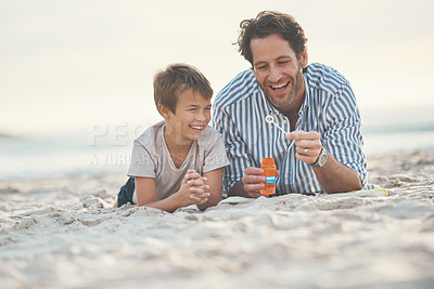 Buy stock photo Full length shot of a playful mature father lying on the beach and blowing bubbles with his son