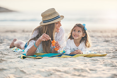 Buy stock photo Full length shot of a playful young mother lying on the beach and blowing bubbles with her daughter