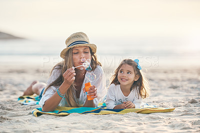 Buy stock photo Full length shot of a playful young mother lying on the beach and blowing bubbles with her daughter