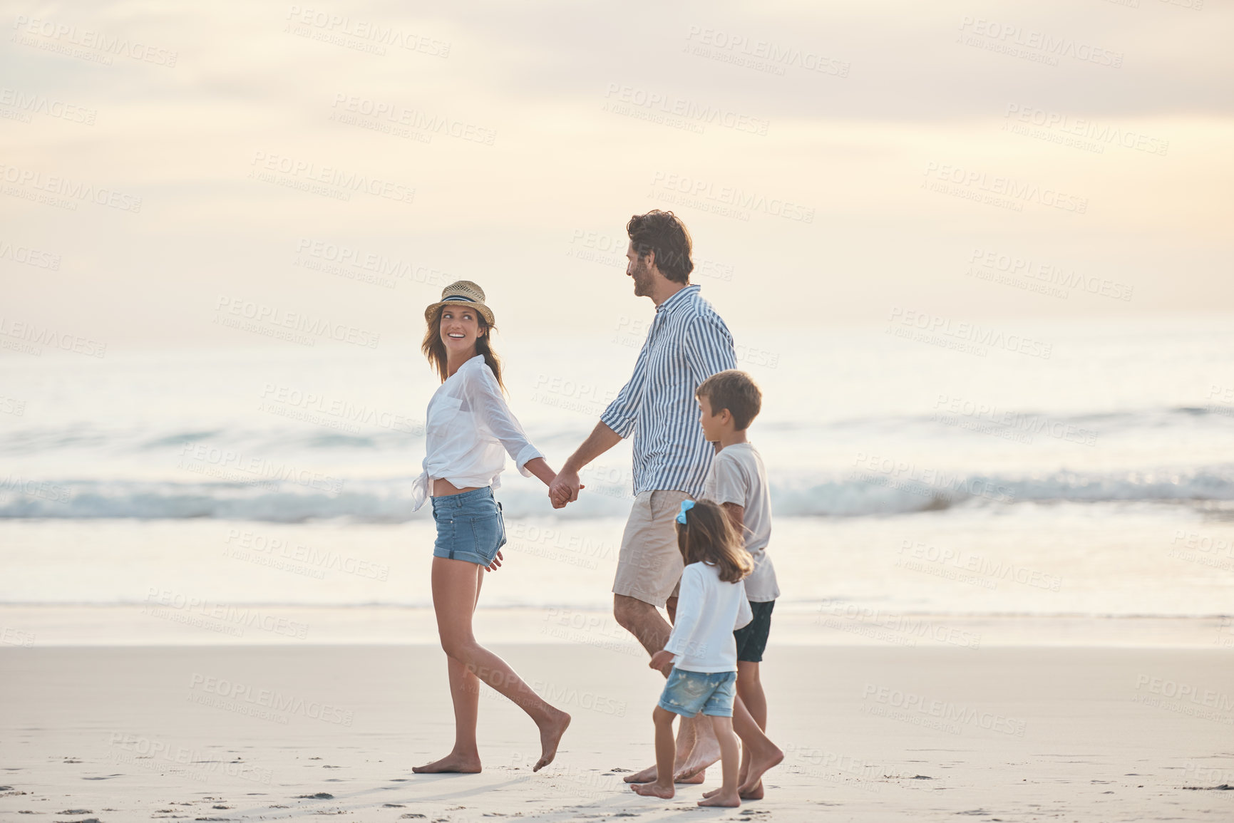 Buy stock photo Full length shot of a happy couple holding hands with their two children and walking along the beach