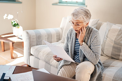 Buy stock photo Shot of a senior woman looking stressed while going through paperwork at home