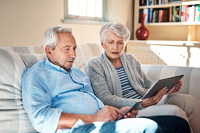 Buy stock photo Shot of a senior couple using their smart devices on the sofa at home