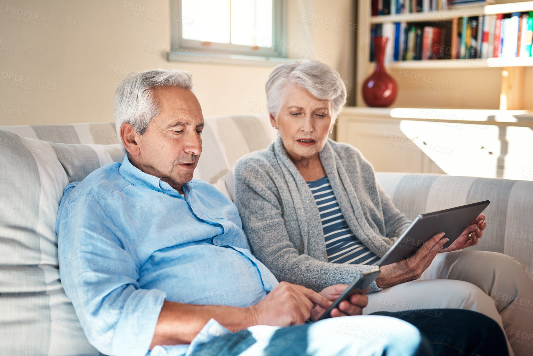 Buy stock photo Shot of a senior couple using their smart devices on the sofa at home