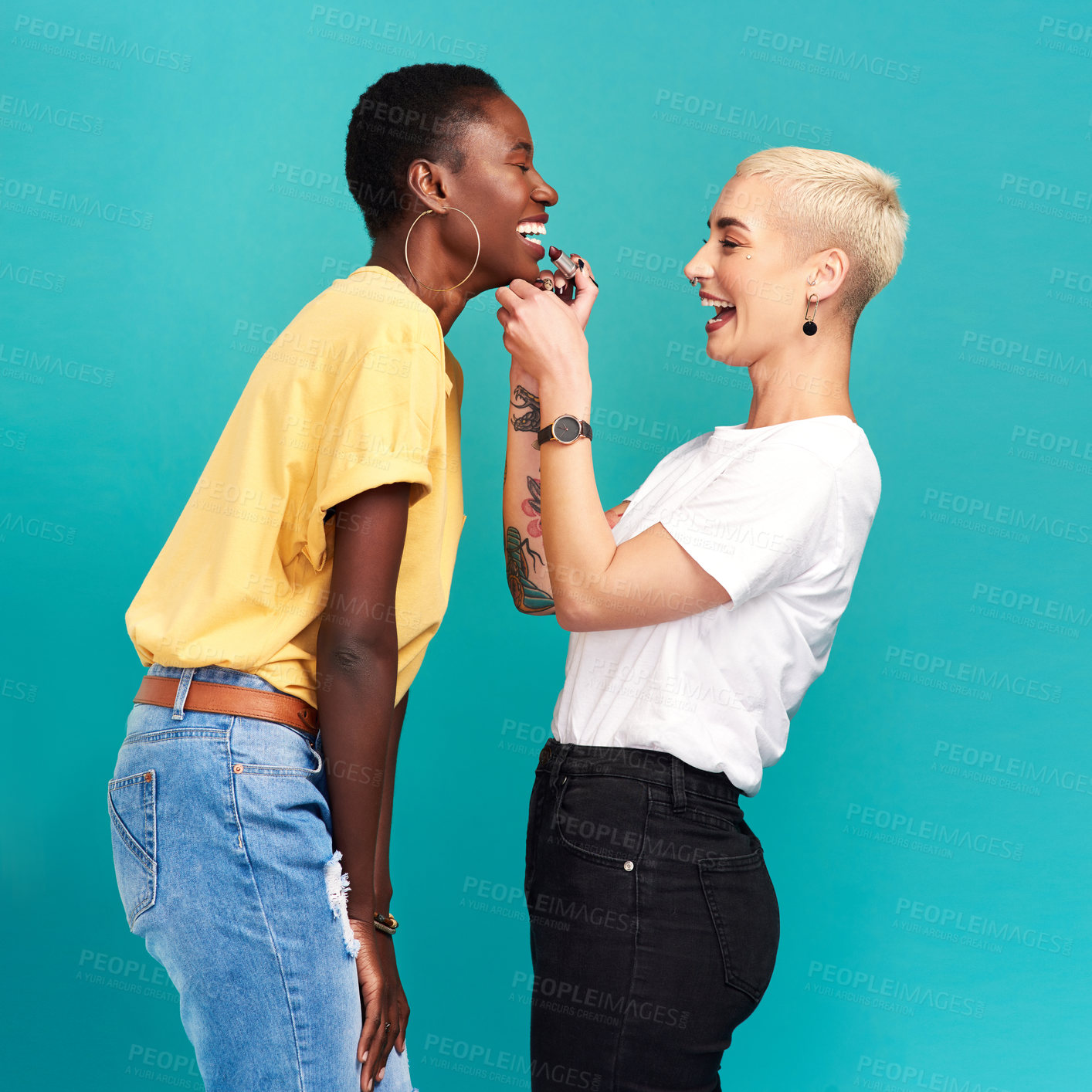 Buy stock photo Studio shot of a young woman putting lipstick on her friend against a turquoise background