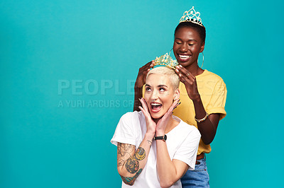 Buy stock photo Studio shot of a young woman putting a crown on her friend against a turquoise background