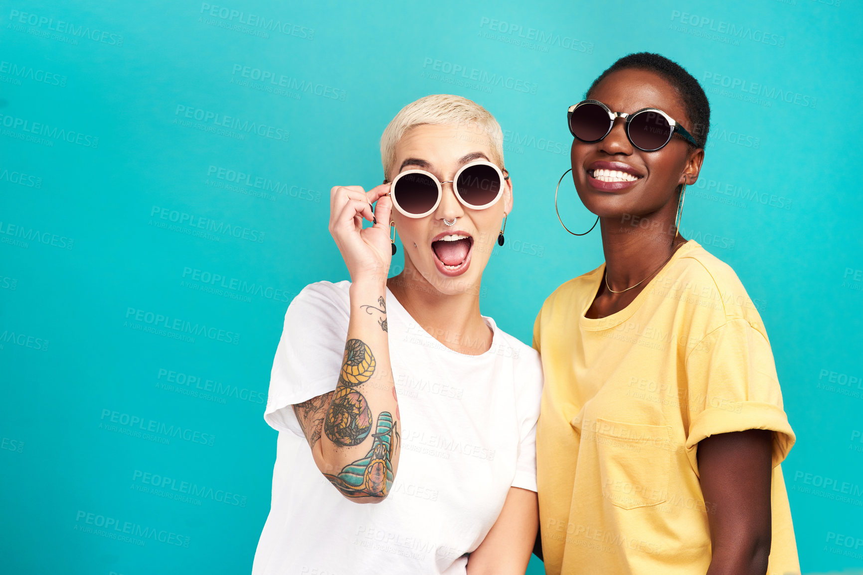 Buy stock photo Studio shot of two young women wearing sunglasses against a turquoise background