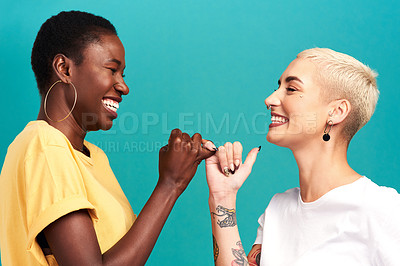 Buy stock photo Studio shot of two young women linking their fingers against a turquoise background