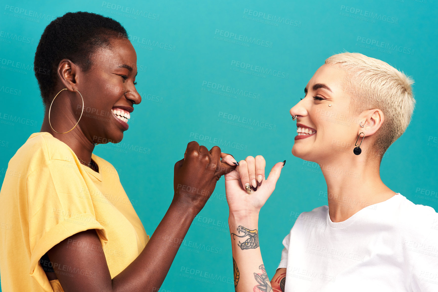 Buy stock photo Studio shot of two young women linking their fingers against a turquoise background