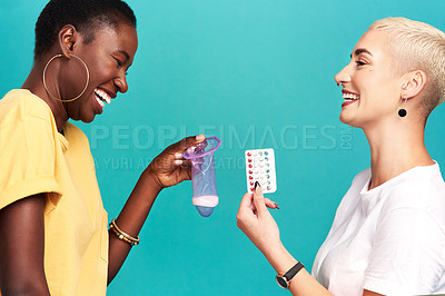 Buy stock photo Studio shot of two young women comparing contraception against a turquoise background