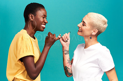 Buy stock photo Studio shot of two young women linking their fingers against a turquoise background