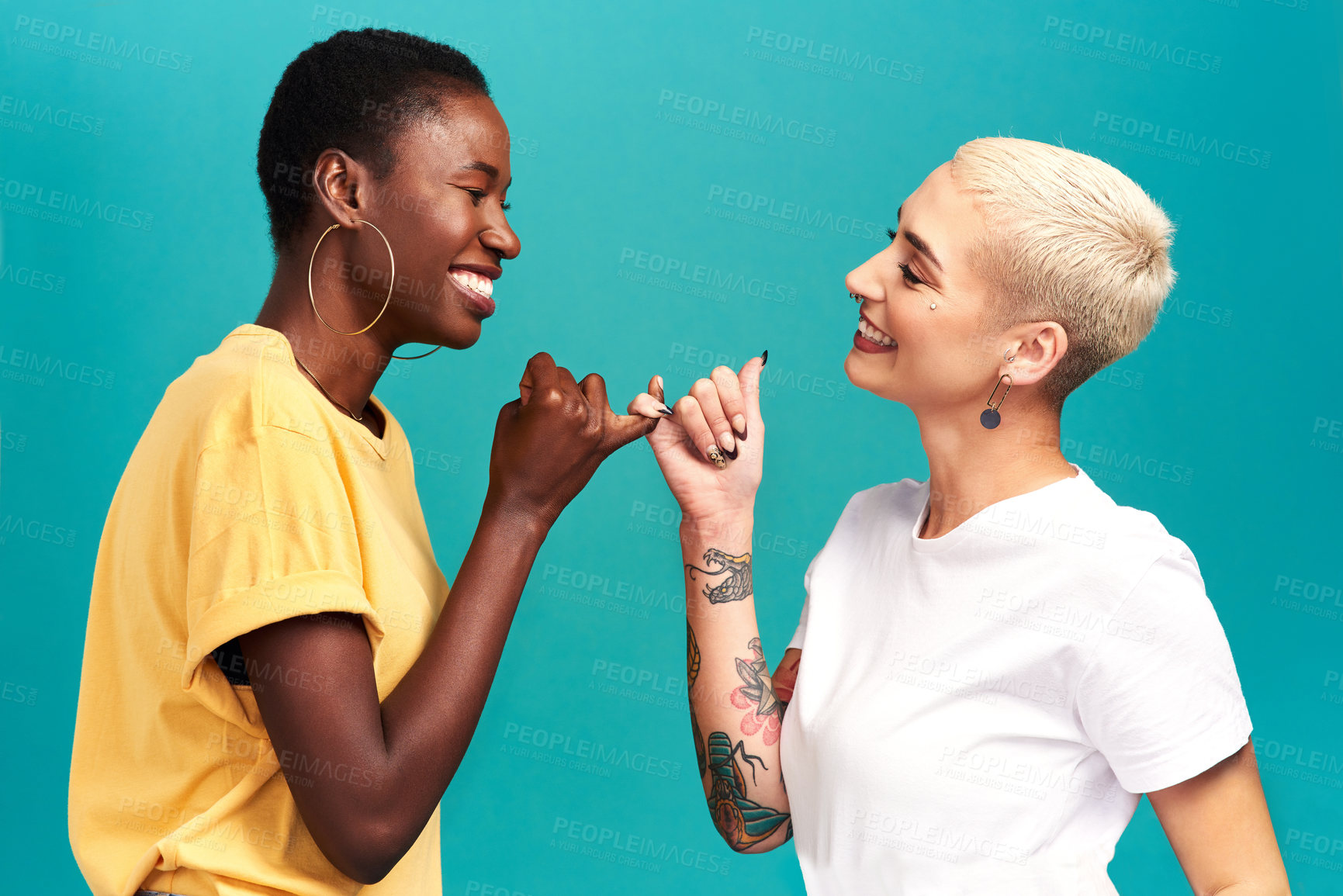 Buy stock photo Studio shot of two young women linking their fingers against a turquoise background